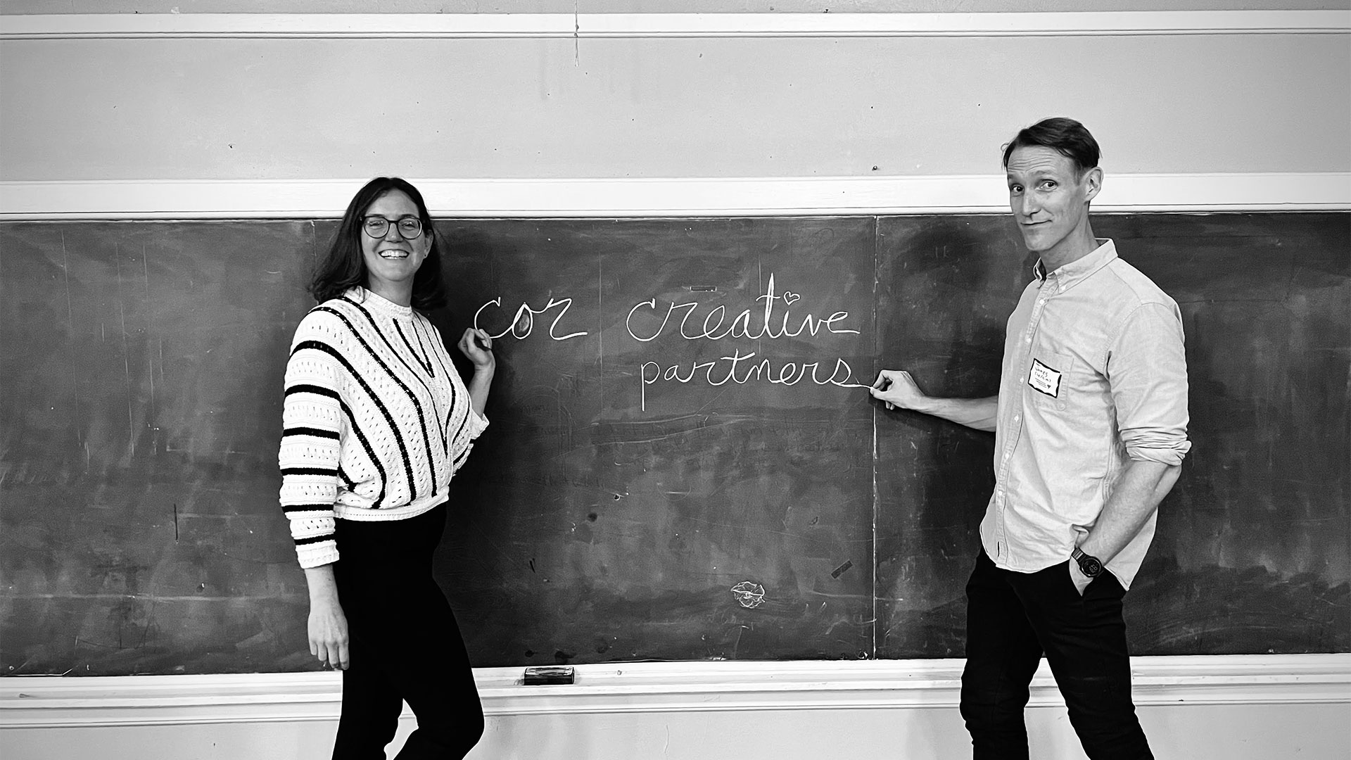 our-story James Simons and Maureen Chapman at a chalkboard with cor creative partners written in cursive